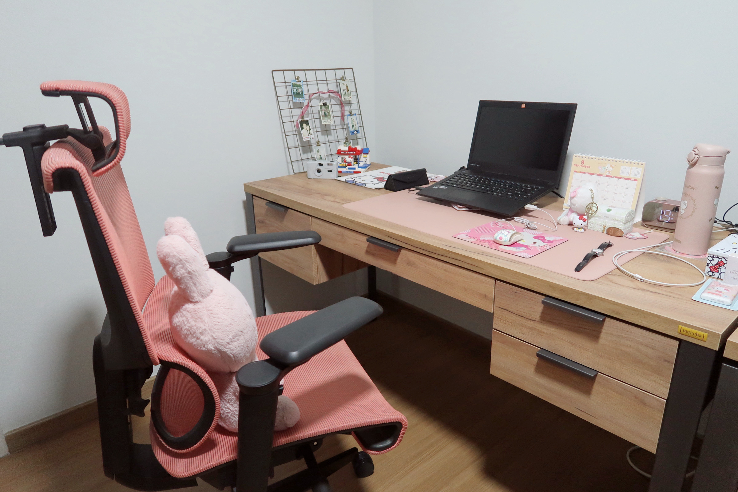 Our work space customised to our needs  - Pink ergonomic office chair, pink plush toy, wooden desk, black laptop, calendar