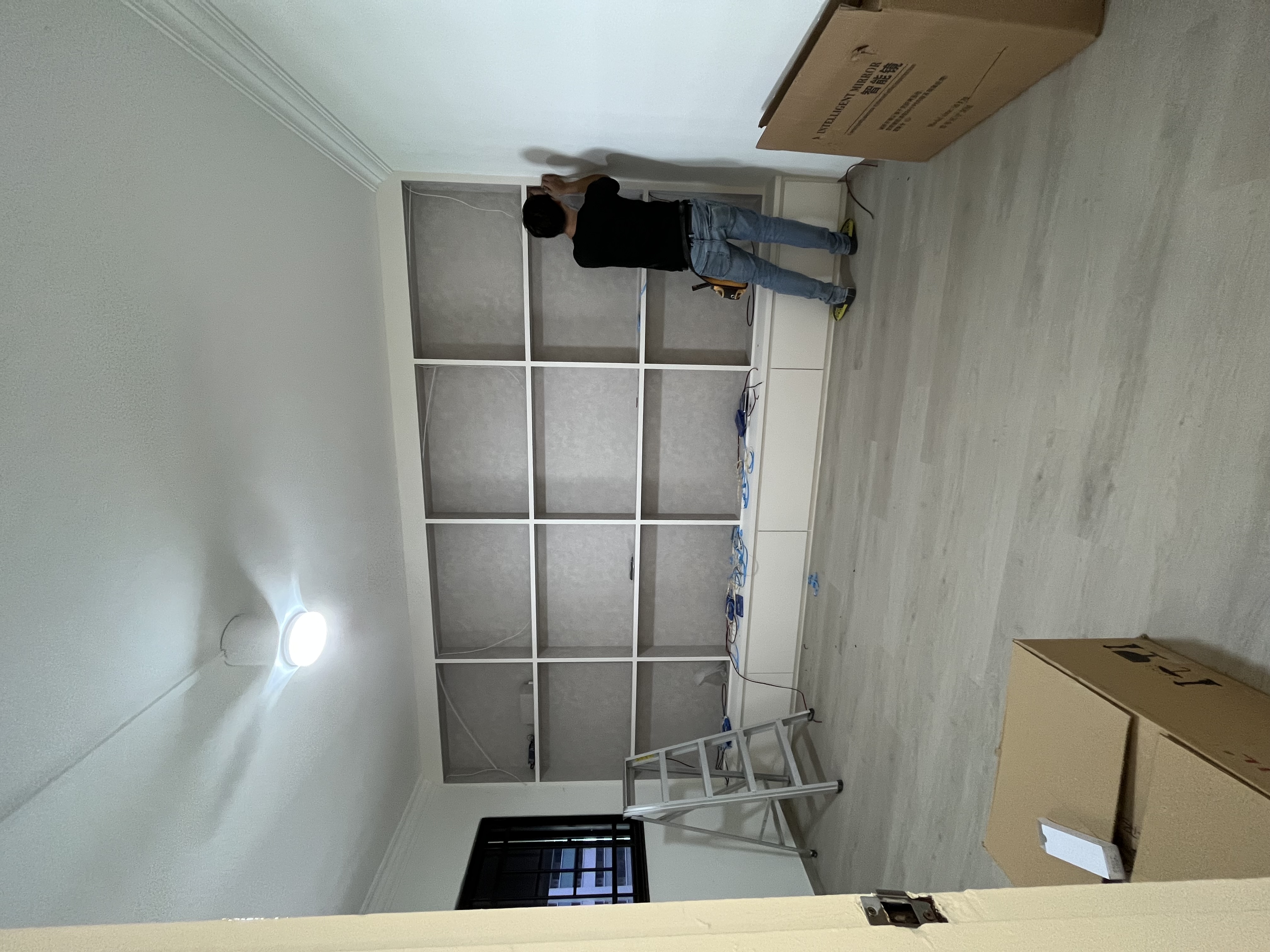 Design the display cabinet of your dreams - white wall, man working, ceiling fan, electrical wires, cardboard box, ladder