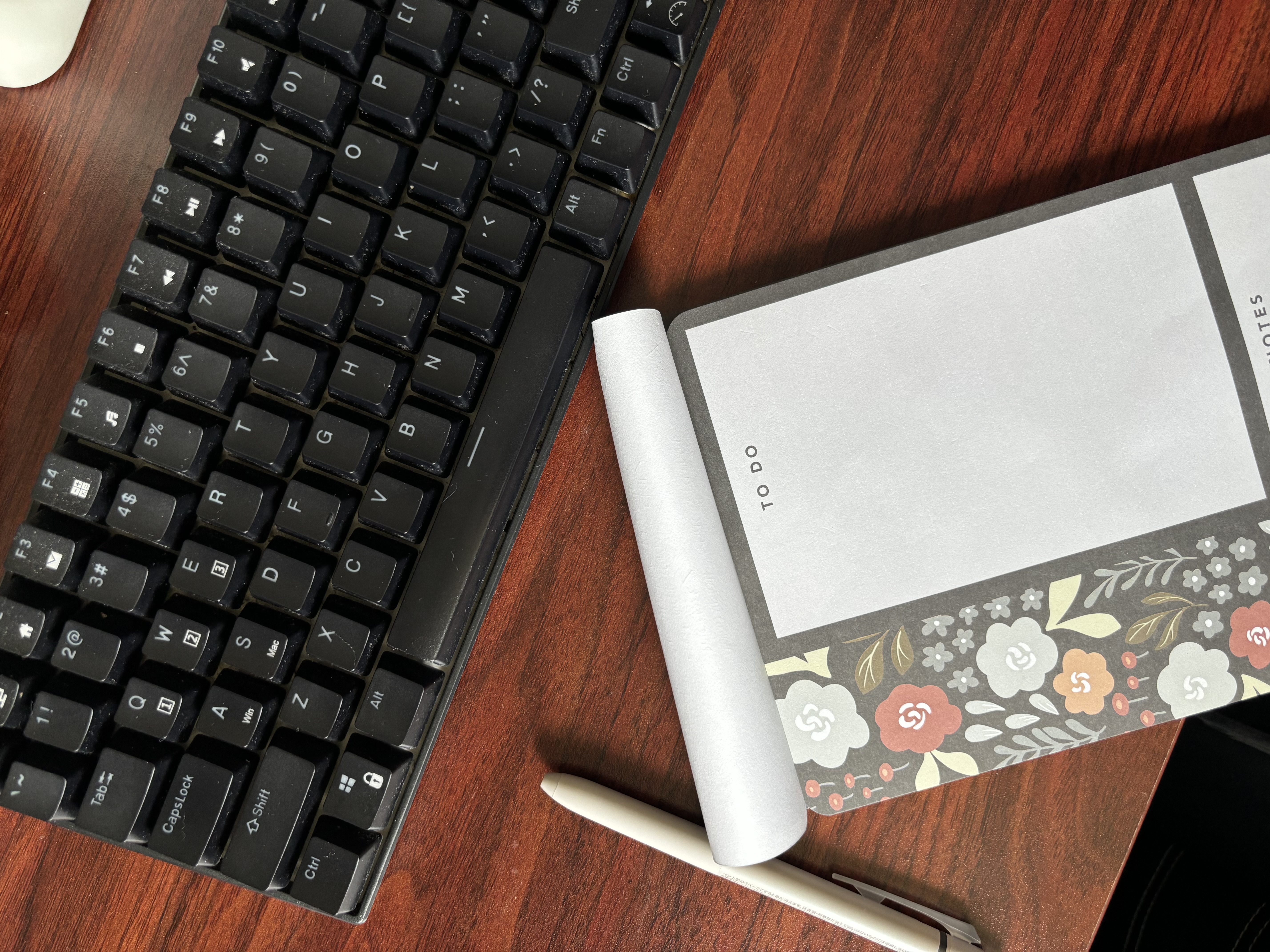 The Ultimate Home Office Experience for the Homebody - Black keyboard, wooden desk, white pen, floral notebook, digital