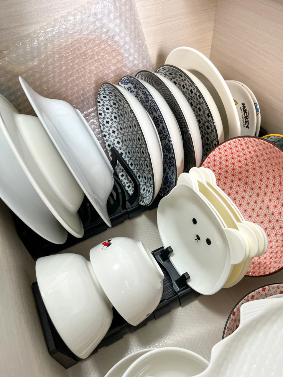A peep into our kitchen cabinets!  - Dishes in various patterns and colors, neatly organized in a storage bin, stacked and