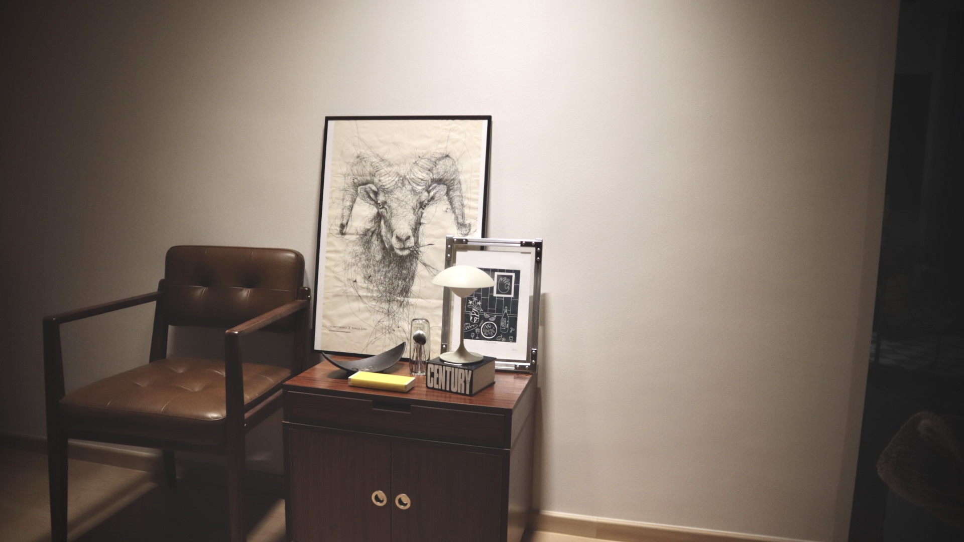 (chair, book, light) maketh nook : trinity to a cosy corner  - Wooden desk, framed artwork, black and white ram illustration