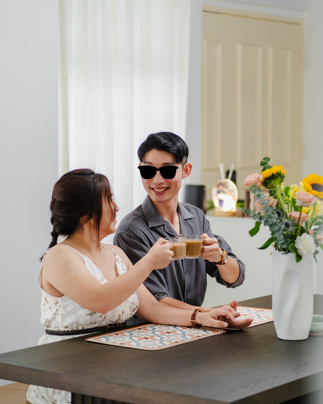 Hosting at Home: From 2 to 22  - Couple sitting at table, holding cups of coffee, smiling, wearing sunglasses, light-colored