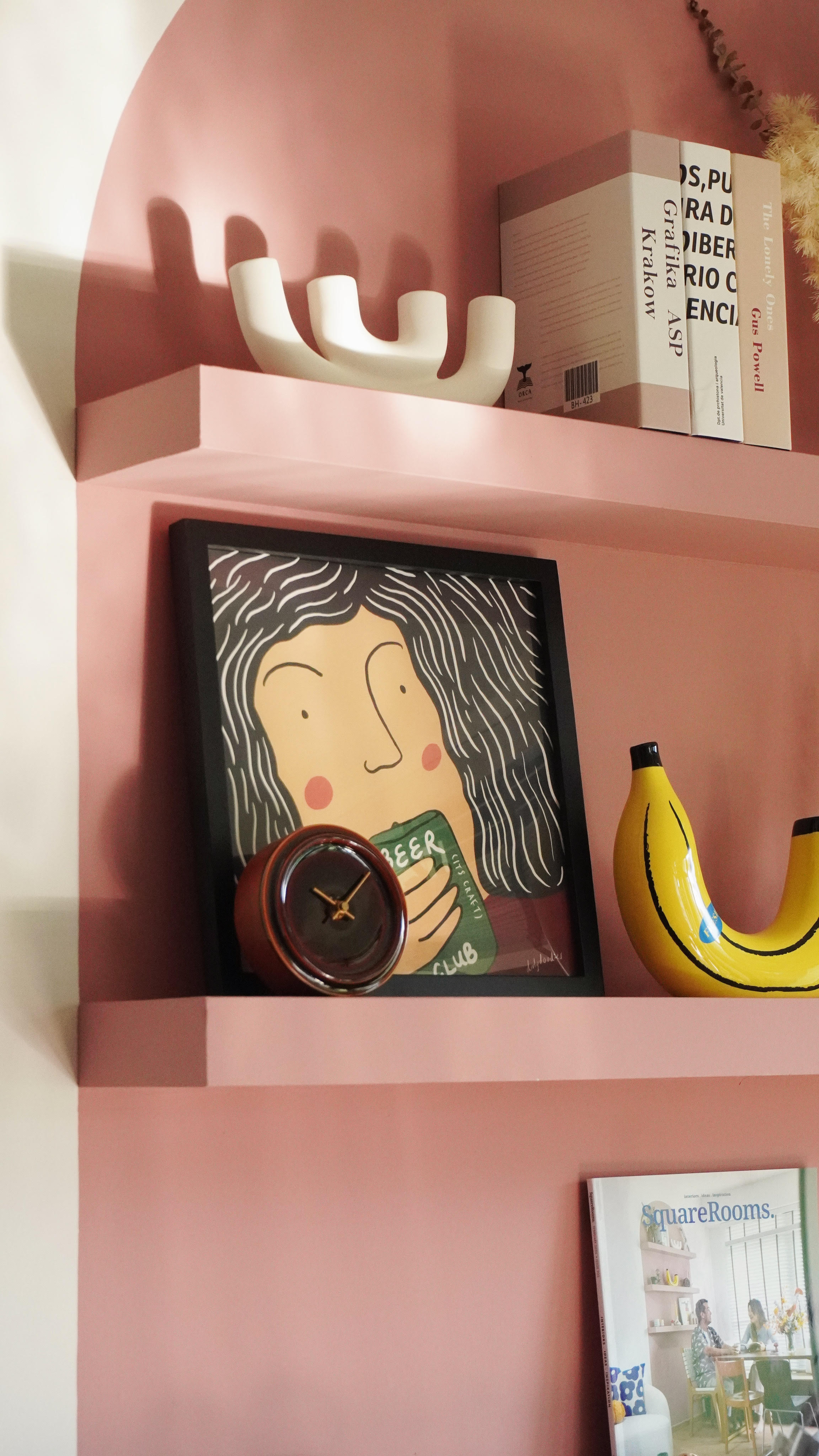 It's the little things that matter. - Pink wall, modern shelf, abstract art, framed picture, cartoonish face, clock, yellow