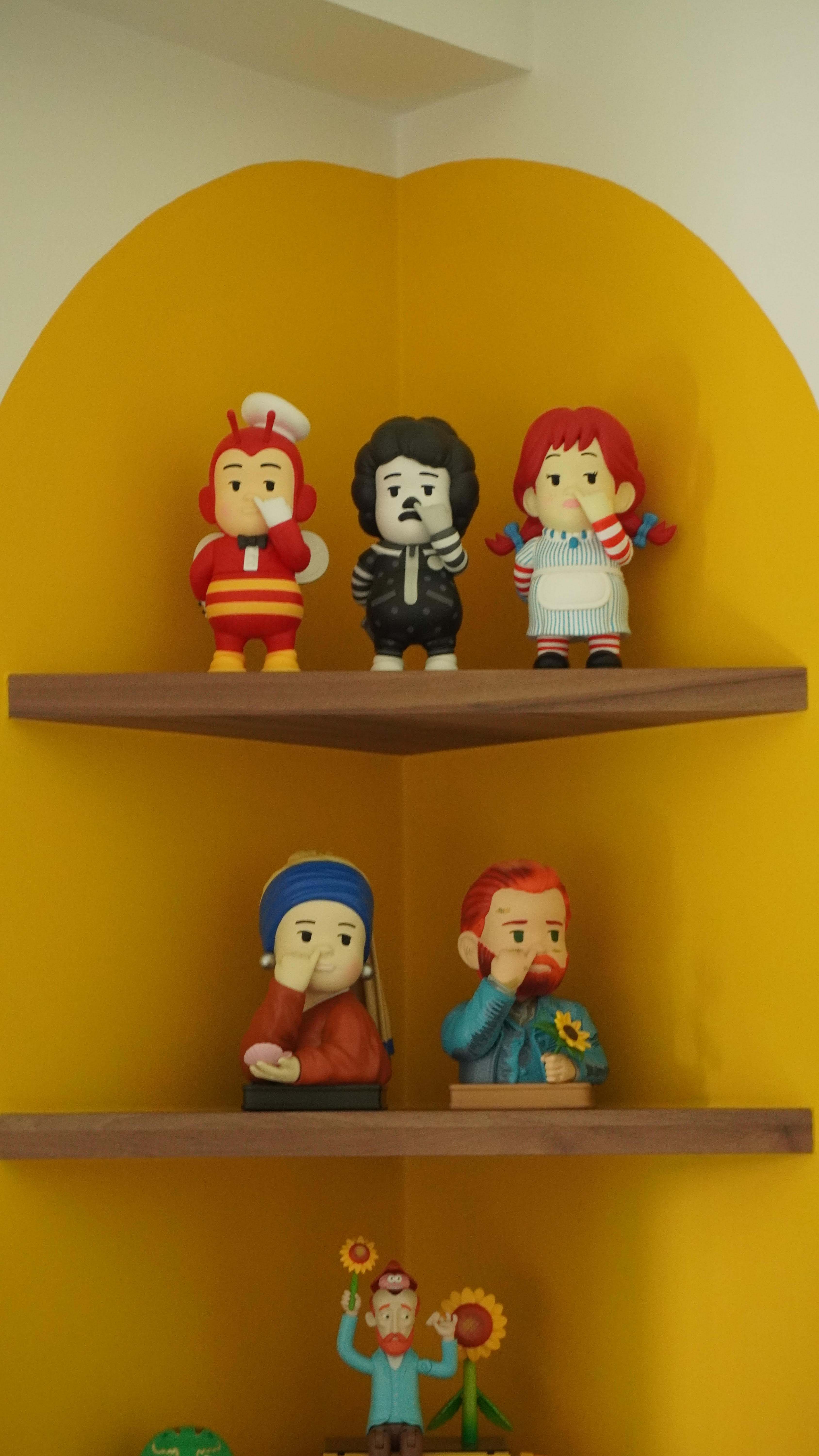 It's the little things that matter. - Cartoon-style figurines on a yellow wall shelf, Three distinct characters with unique