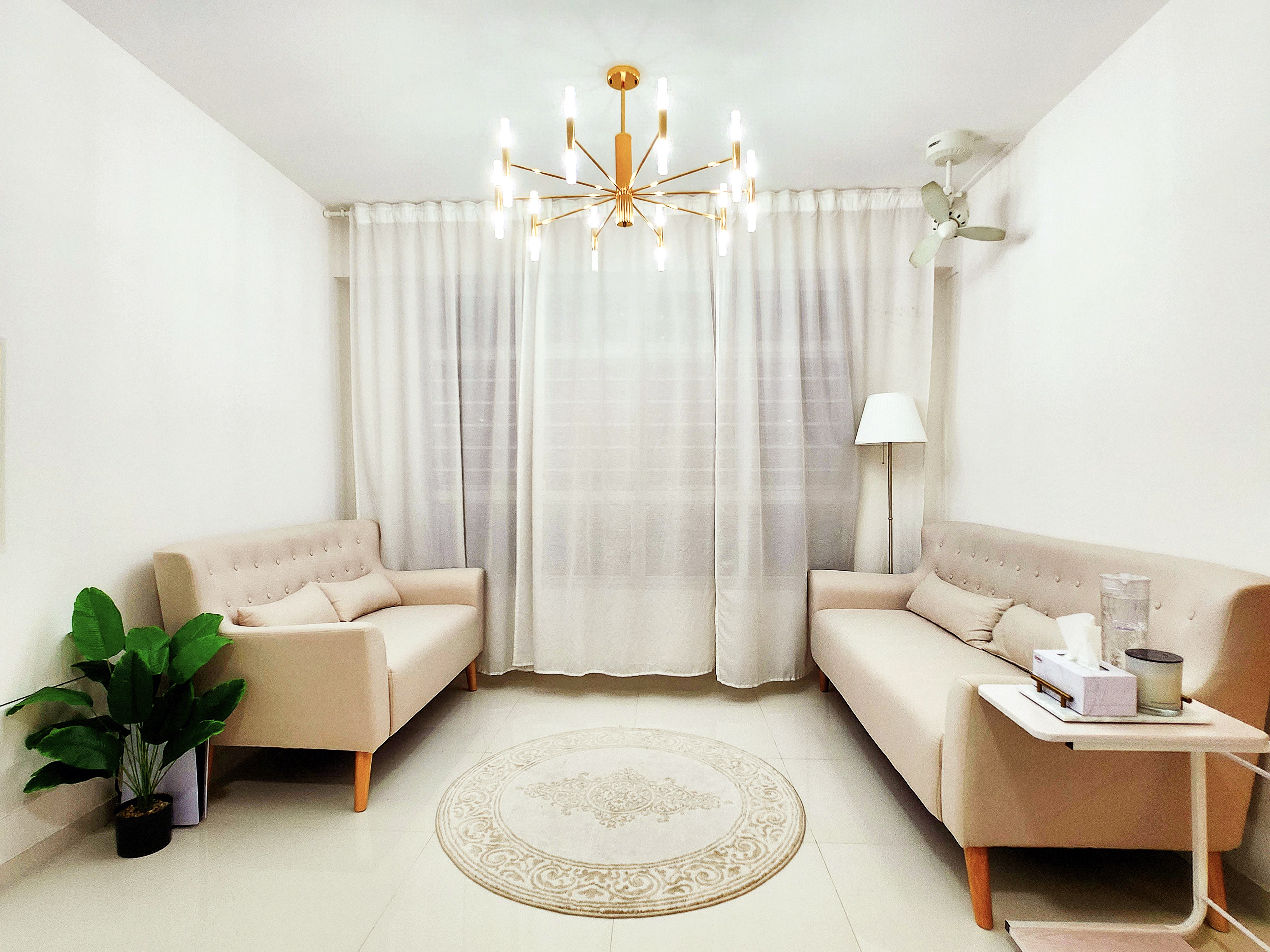 Lightings by punggoHField - Cream-colored sofa, beige cushions, elegant chandelier, white curtains, modern ceiling fan, floor