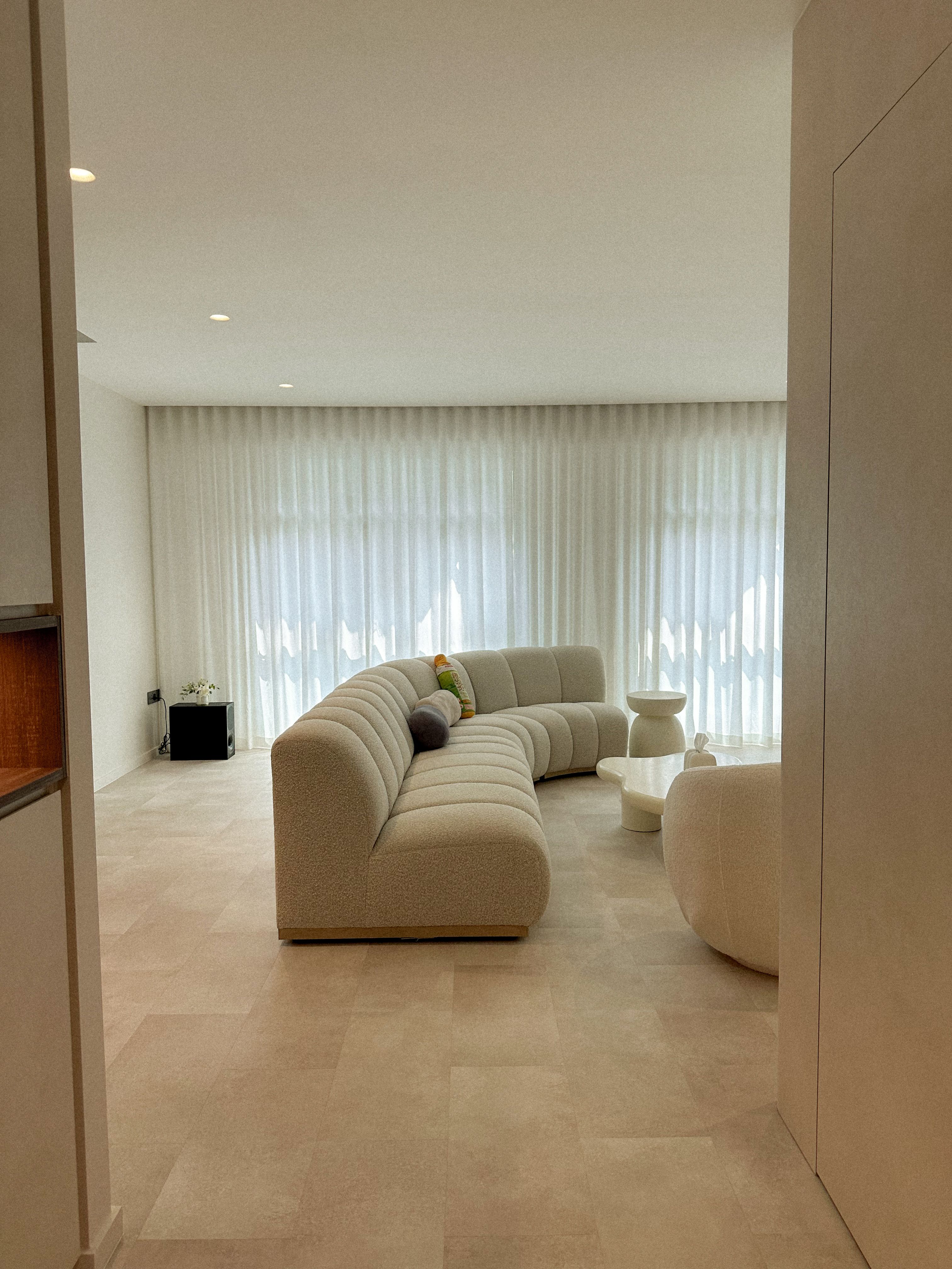 The Big Living Room Theory 📺 - Modern minimalist living room, beige sectional sofa, soft natural light, large window, sheer