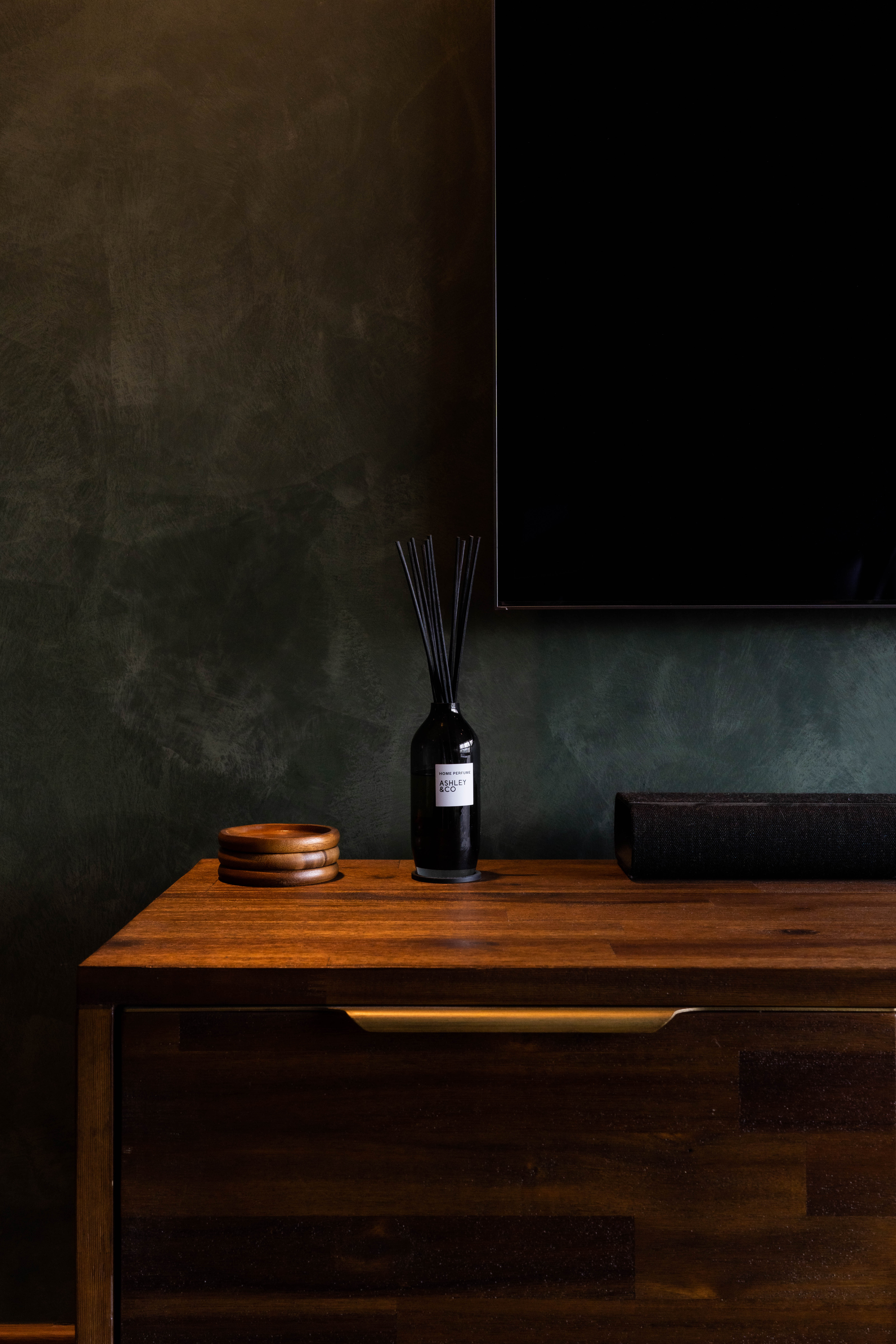 The living - Dark green textured wall, minimalist decor, wooden dresser, sleek black vase, tall wooden plates, cylindrical