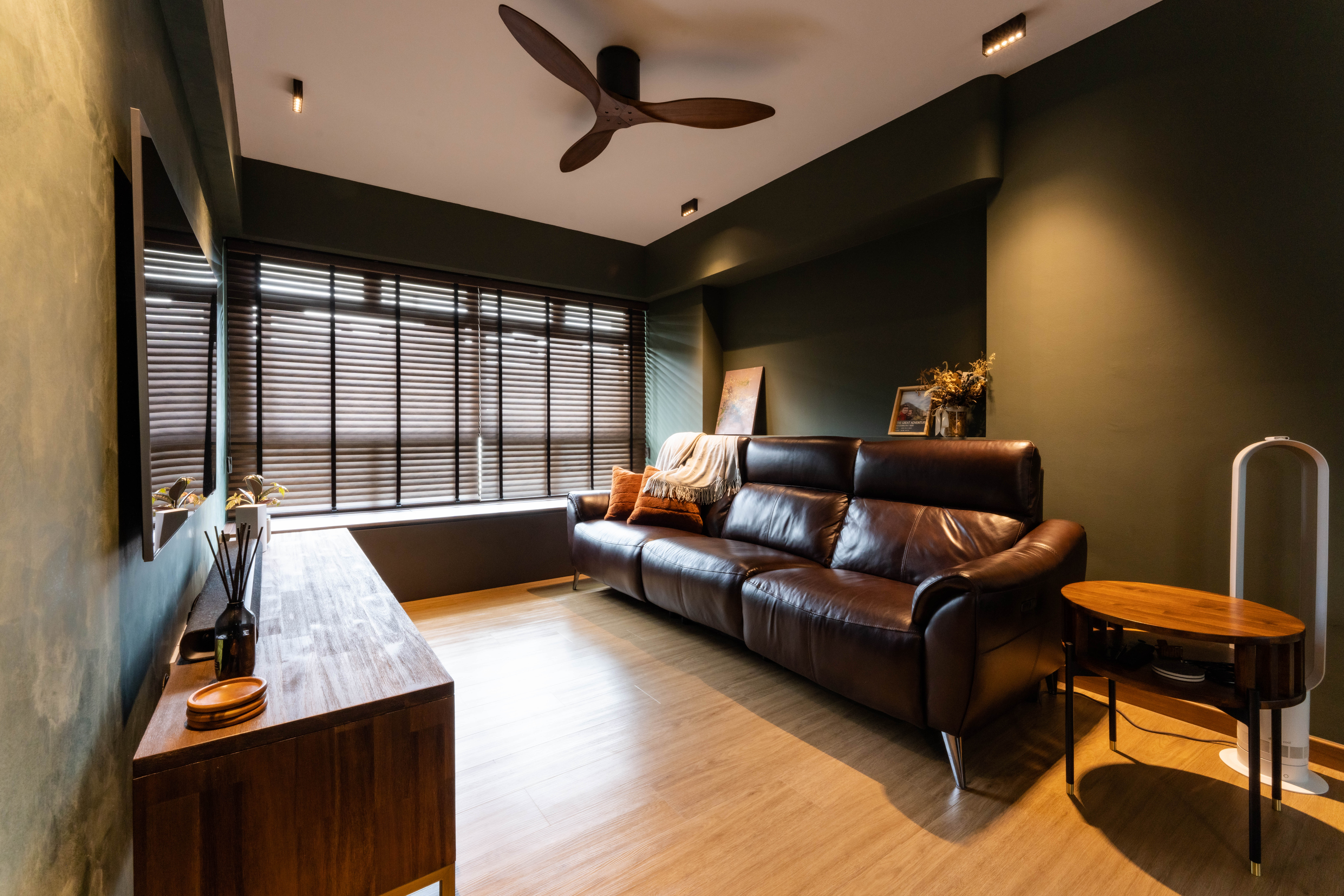 The living - Modern living room with dark green walls, wooden floor, large window with blinds, brown leather sofa, wooden