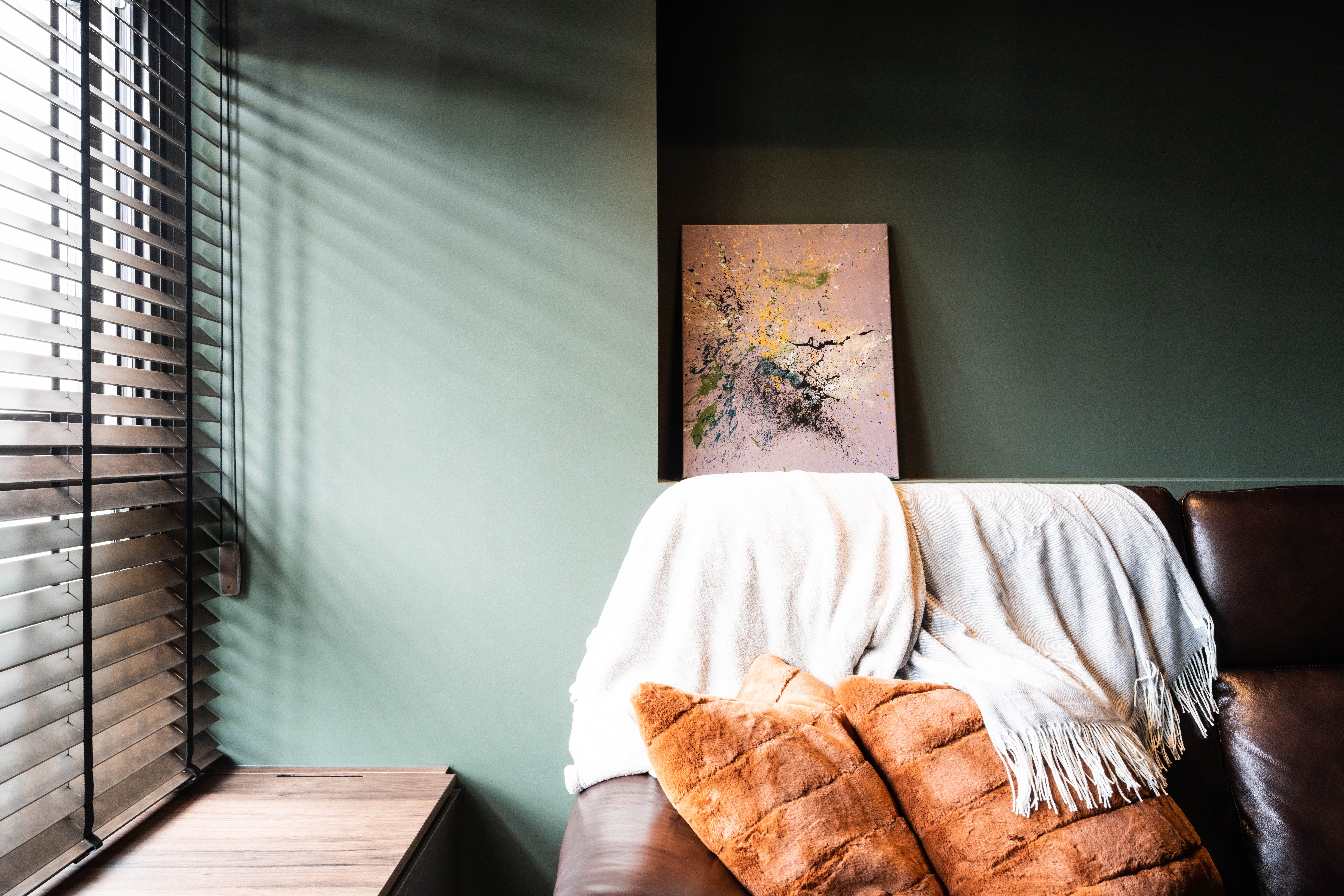 The living - Window with blinds casting shadows, light streaming through, light-colored wall, abstract painting on wall