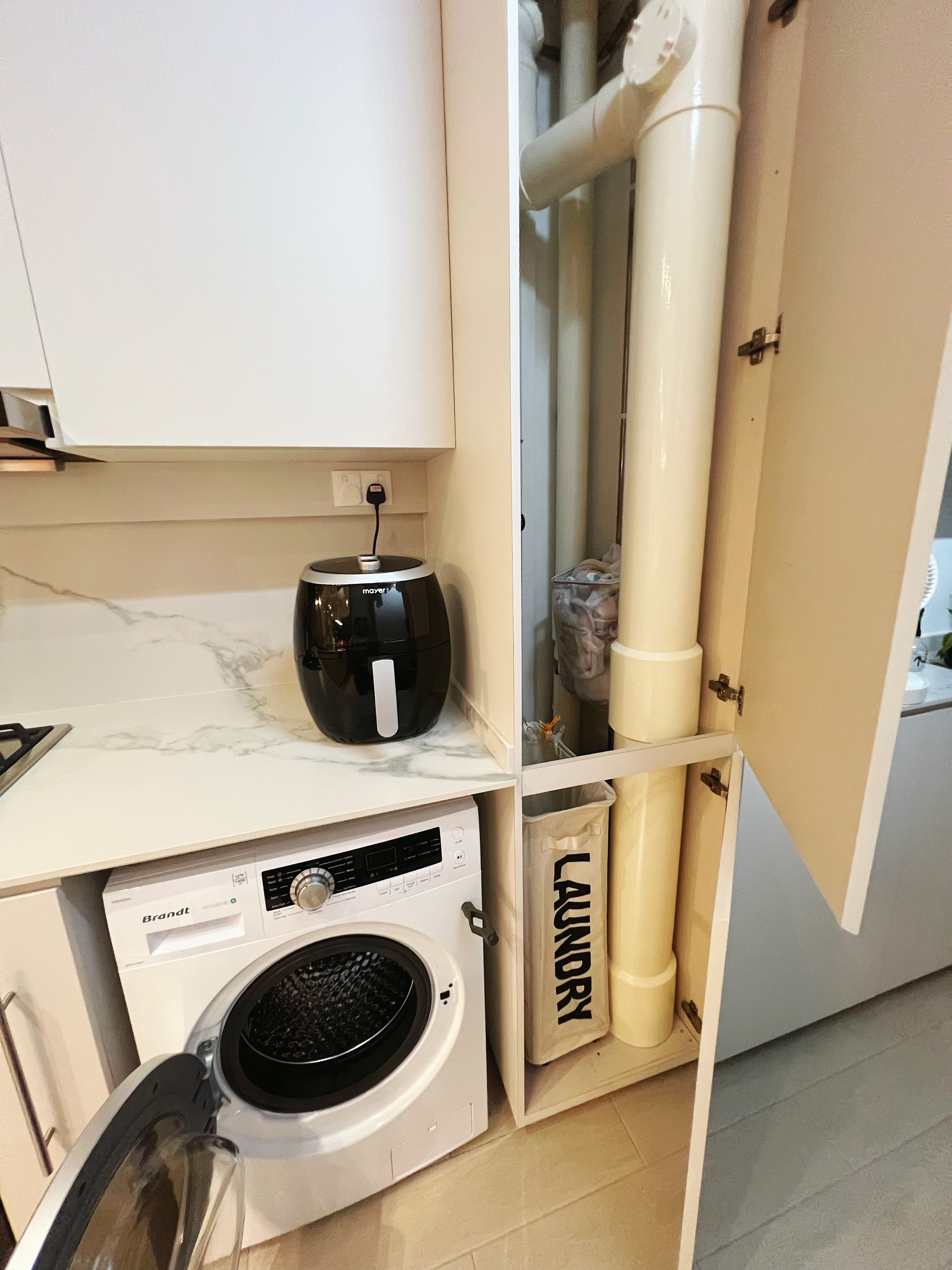 An all white kitchen separated  into wet and dry areas - microwave, washing machine, laundry basket, white cabinets, marble