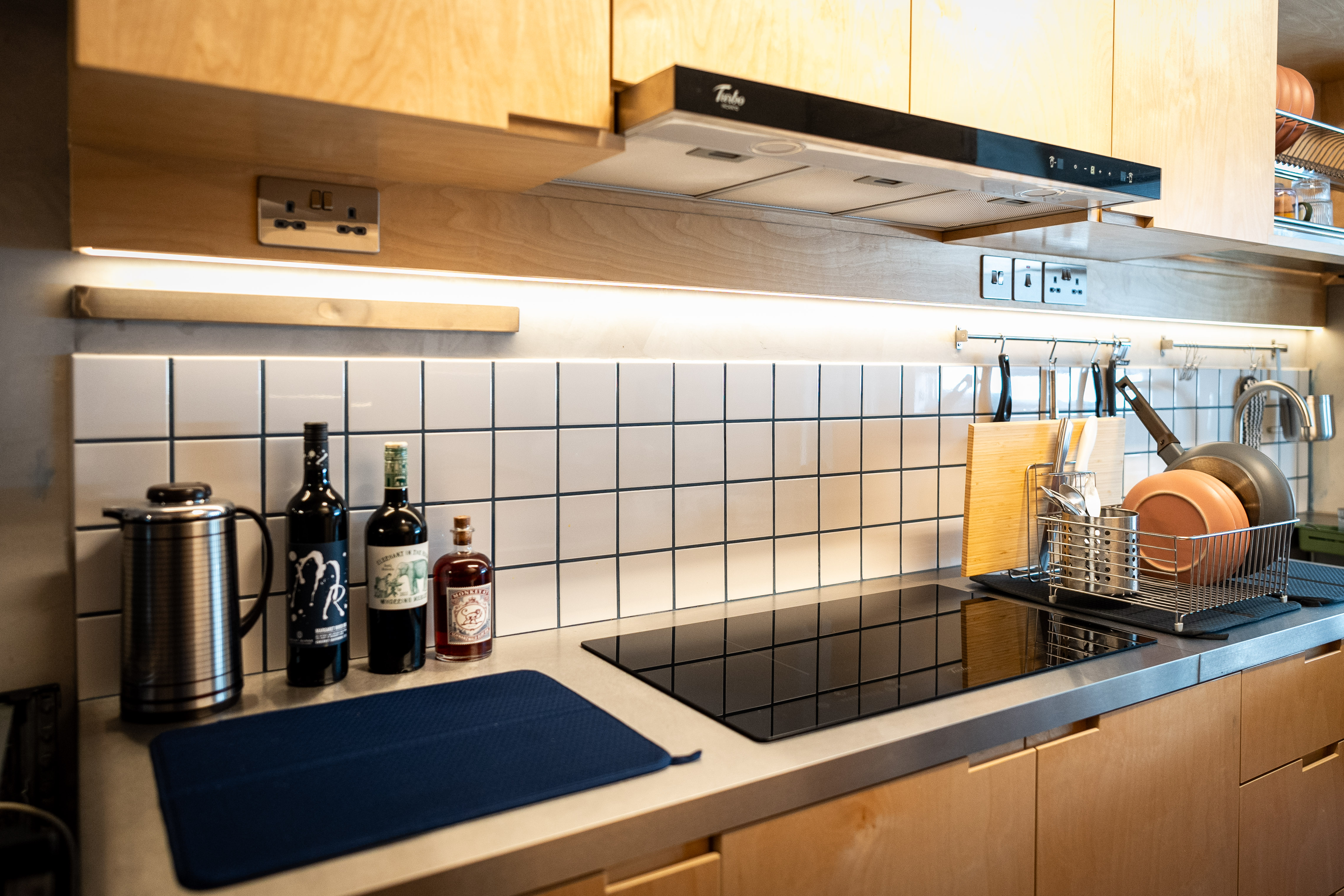 A Coffee Lover's Spacious & Charming Kitchen - Wooden cabinets, stainless steel kettle, black stove, white tiled backsplash