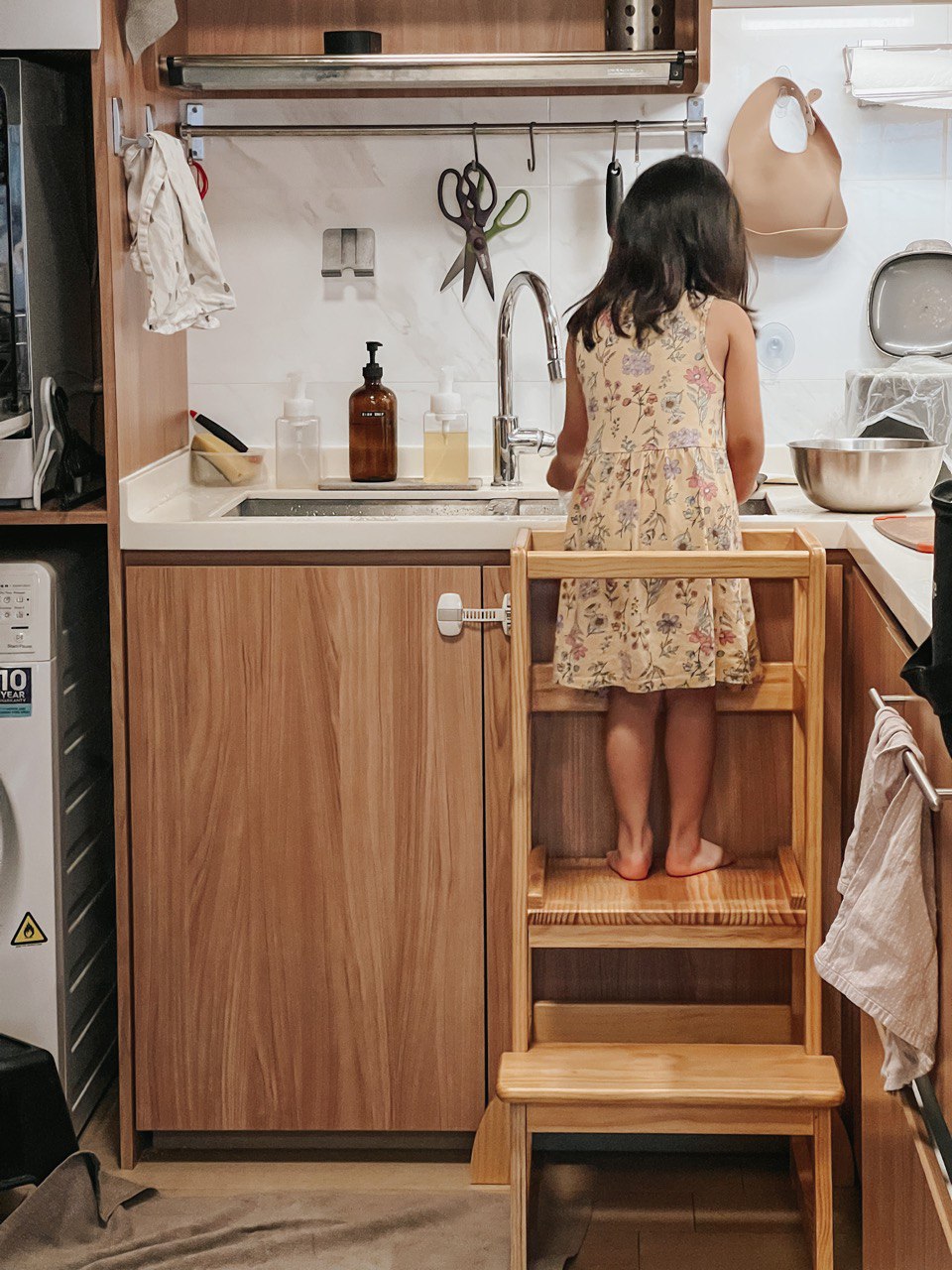 A Compact, Kid-Friendly Kitchen Without a Service Yard - Wooden kitchen cabinet, young girl washing dishes, wooden stool