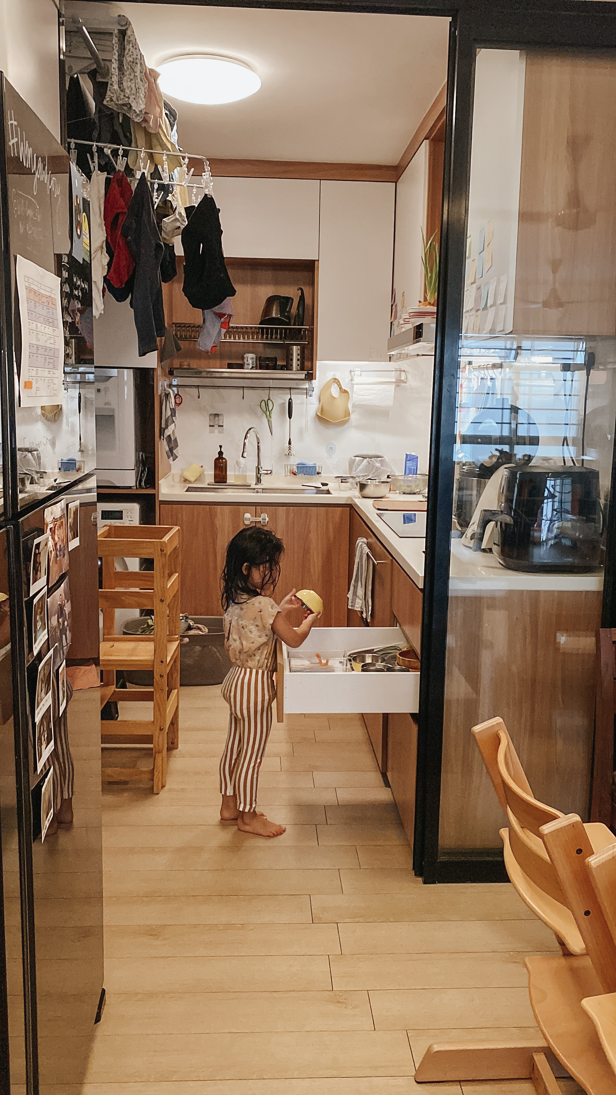 A Compact, Kid-Friendly Kitchen Without a Service Yard - kitchen, child, open drawer, clothes, wooden stools, refrigerator