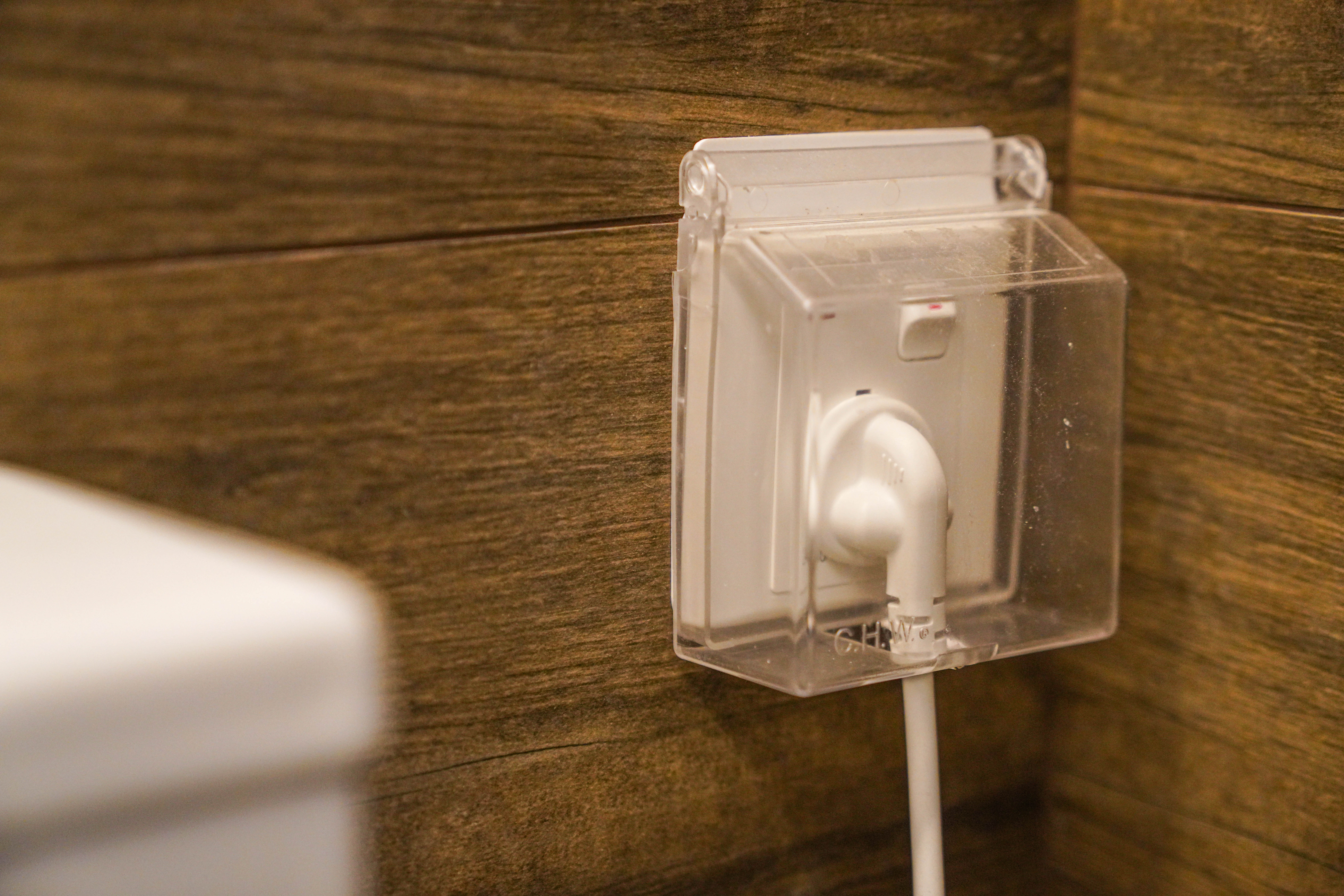 Resort-like Common Bathroom (+Smart Toilet @ $450) - Clear plastic box, white charging cable, wooden wall, bathroom setting