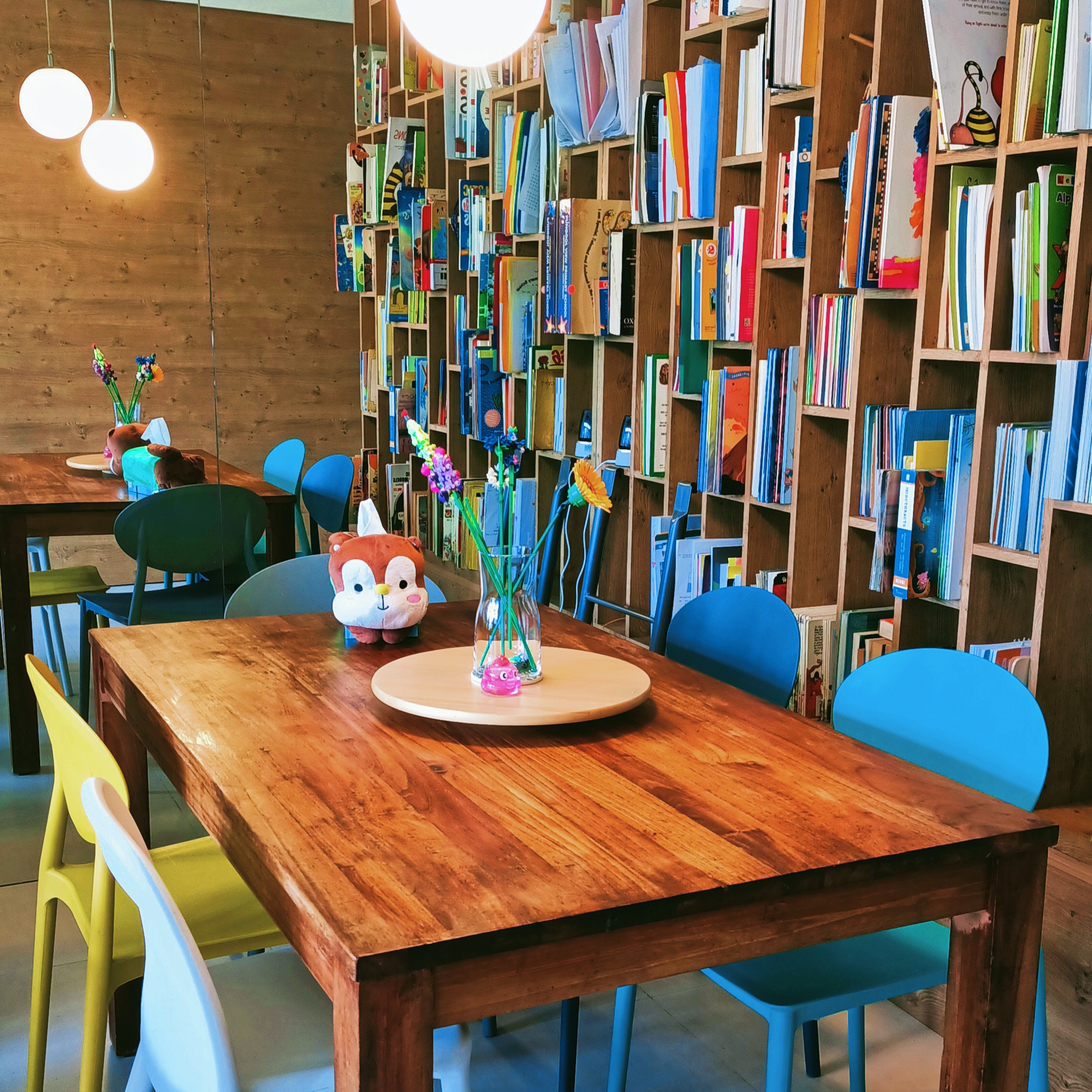 26K Cozy Rustic Home with Swing and Study Corridor - Wooden bookshelf filled with colorful books, wooden table with a vase of