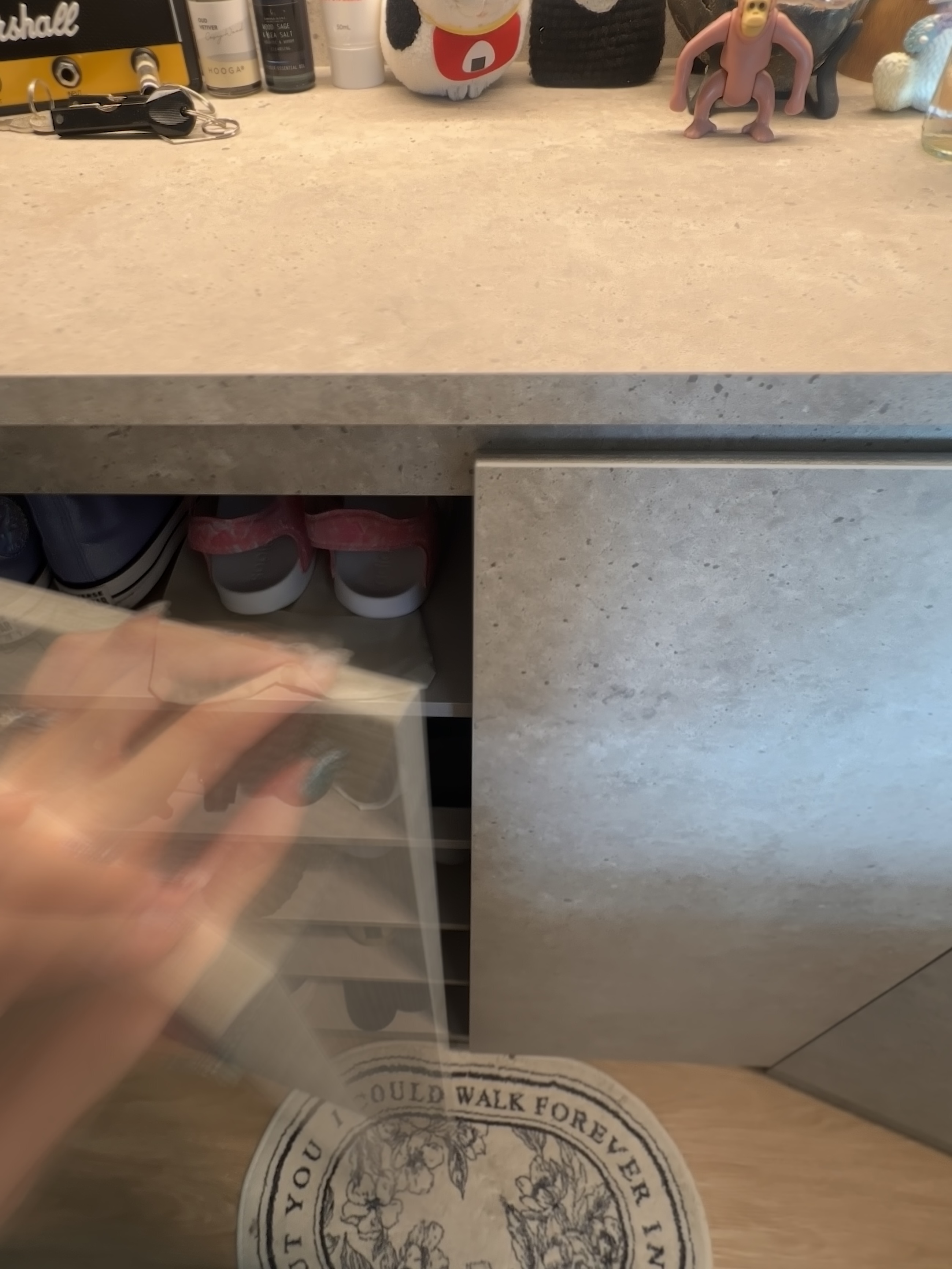 Entryway That Speaks Minimalism & Modern Life - Underneath the countertop, a pair of sneakers is visible., A hand reaches