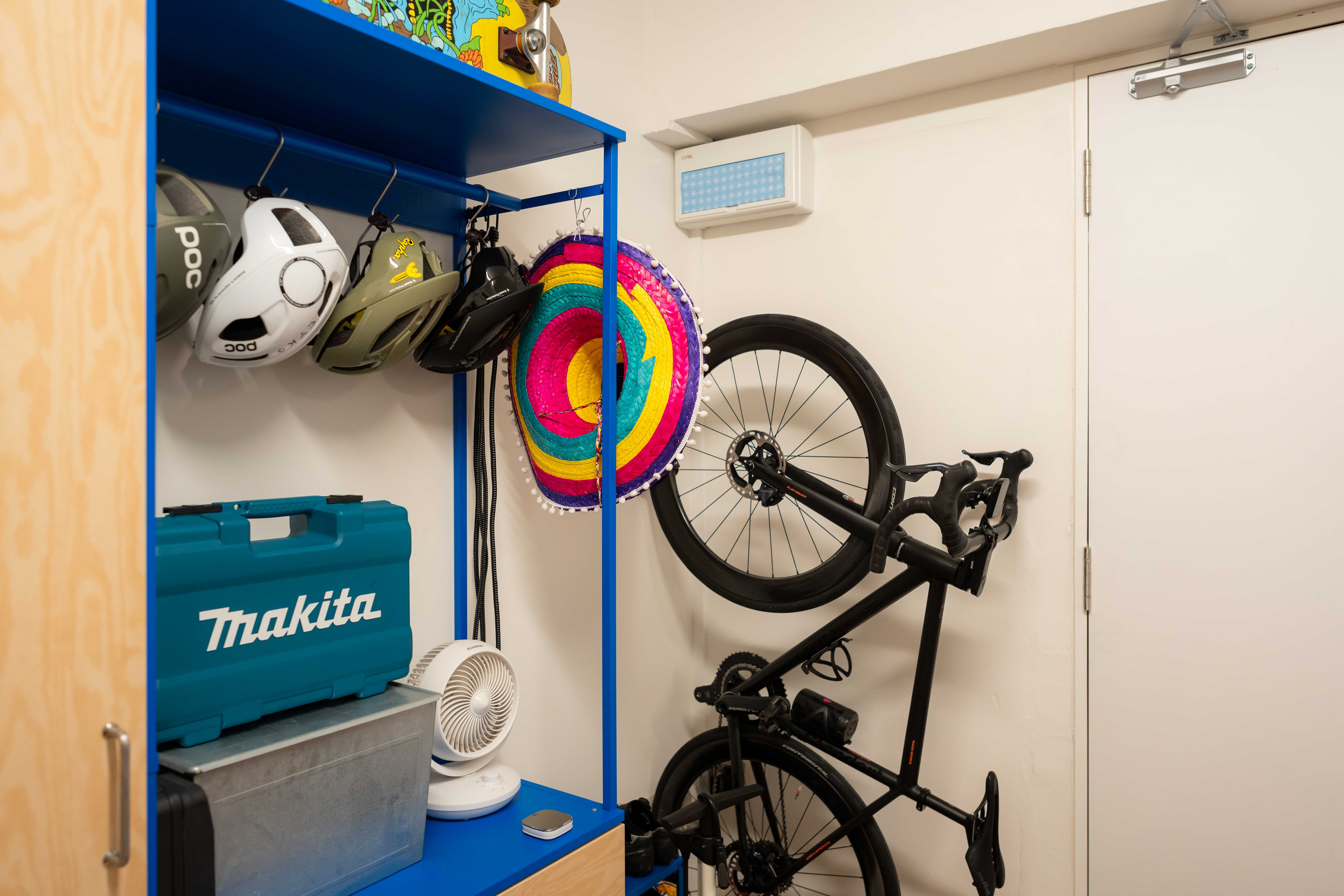 A colourful entryway with vibrant hues and a sporty vibe! - blue shelving unit, bicycle, colorful helmet, white fan, black