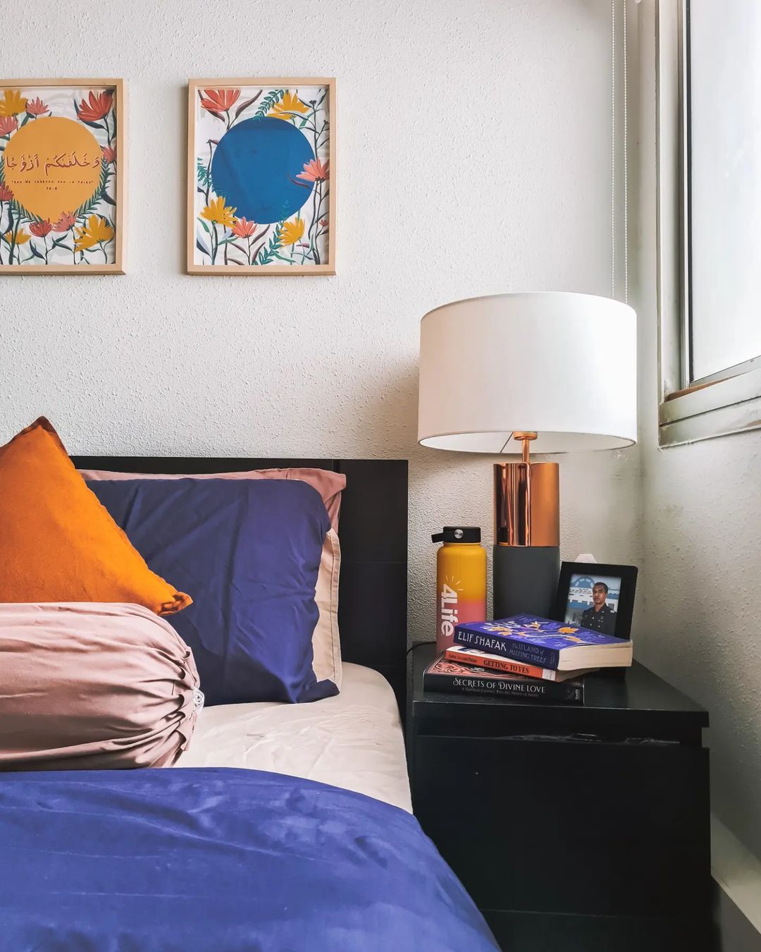 Cosy Colour Pop Bedroom - Floral frame, vibrant pillows, orange and blue bedding, modern lamp, bookshelf, personal items