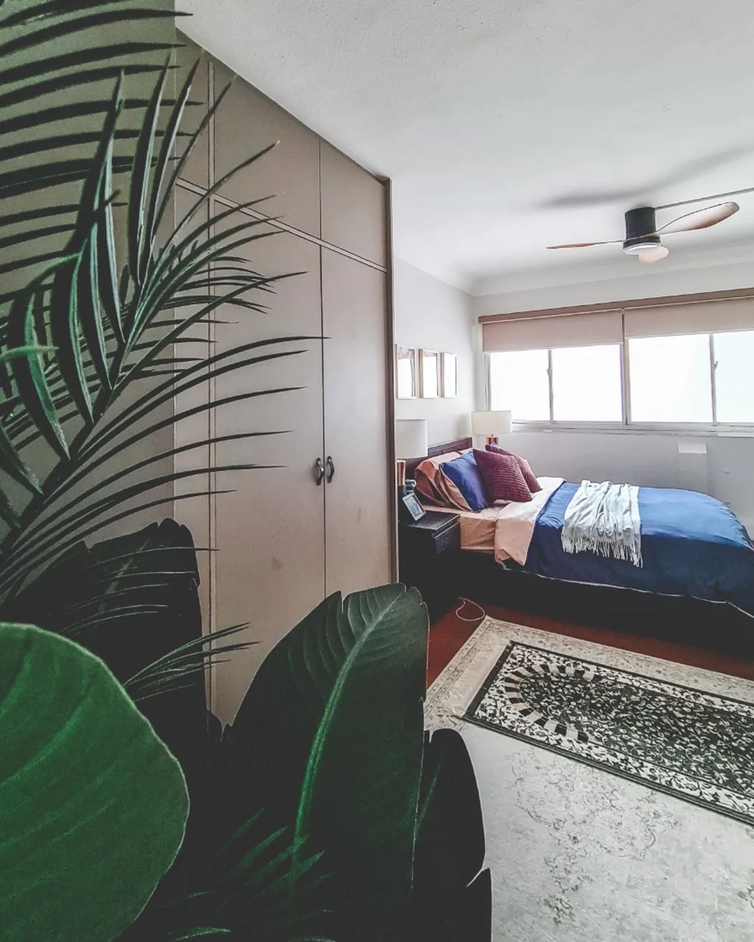 Cosy Colour Pop Bedroom - Leather wardrobe, large green plant, patterned rug, cozy bed, blue and pink bedding, white lamp