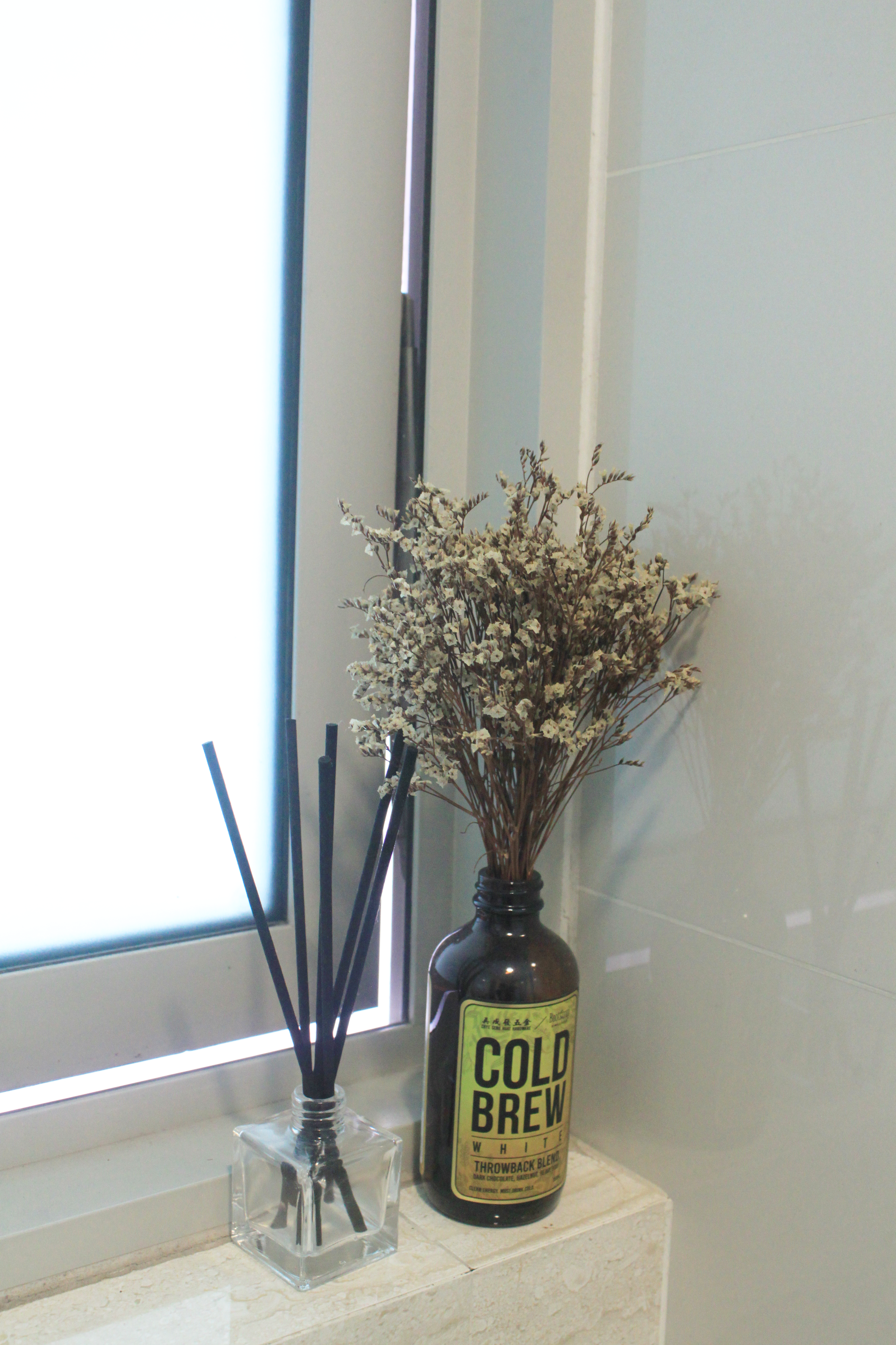My Home Away From Home - vase with black sticks, white flowers, clear glass bottle, "Cold Brew White" label, bathroom