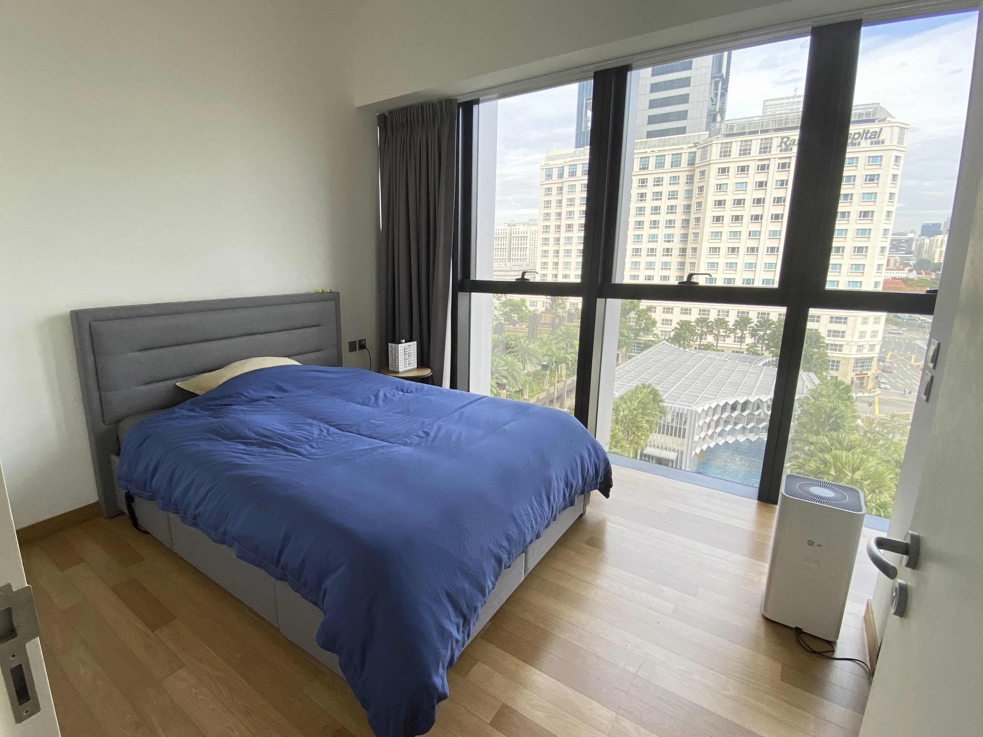 A Photographer's One-Room Studio Man Cave - Modern bedroom with large window, blue bedspread, gray headboard, wooden floor