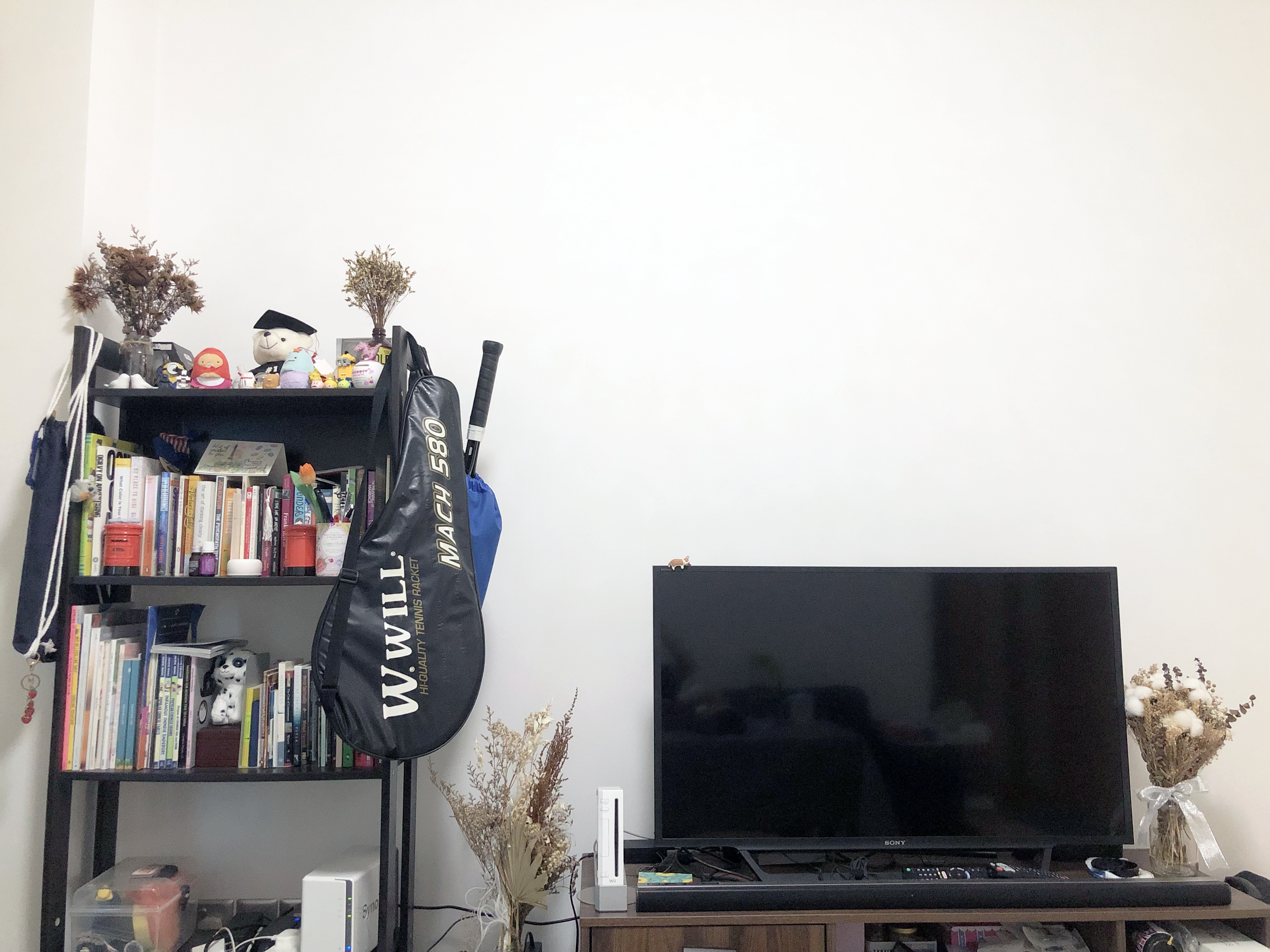 My Home Away From Home - Bookshelf, decorative items, TV stand, black sports bag, tennis racket, remote control, vase with