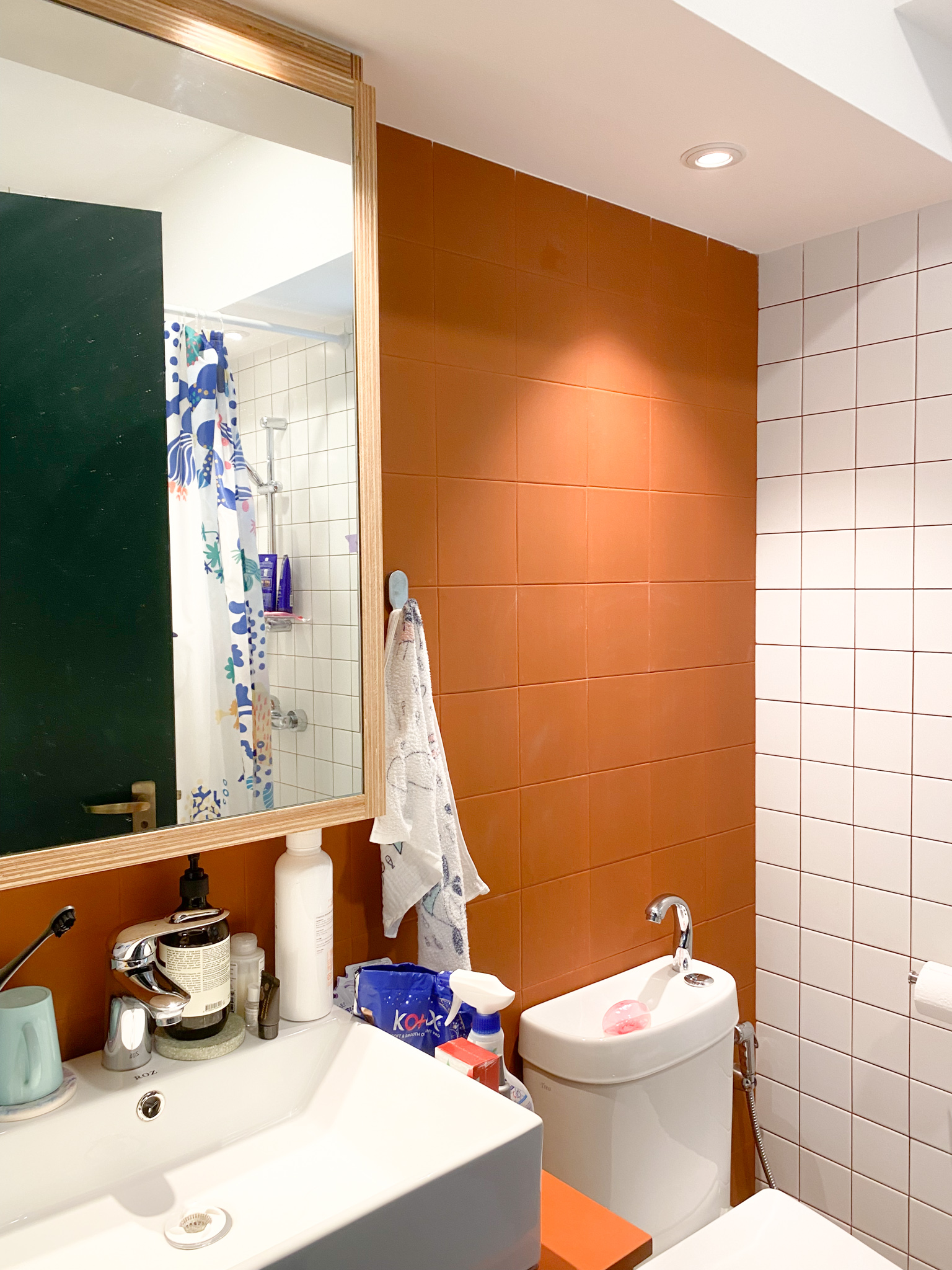 The Eccentricity of an Artistic Couple’s Apartment - Orange bathroom tiles, white tiled wall, mirror frame, bathroom sink
