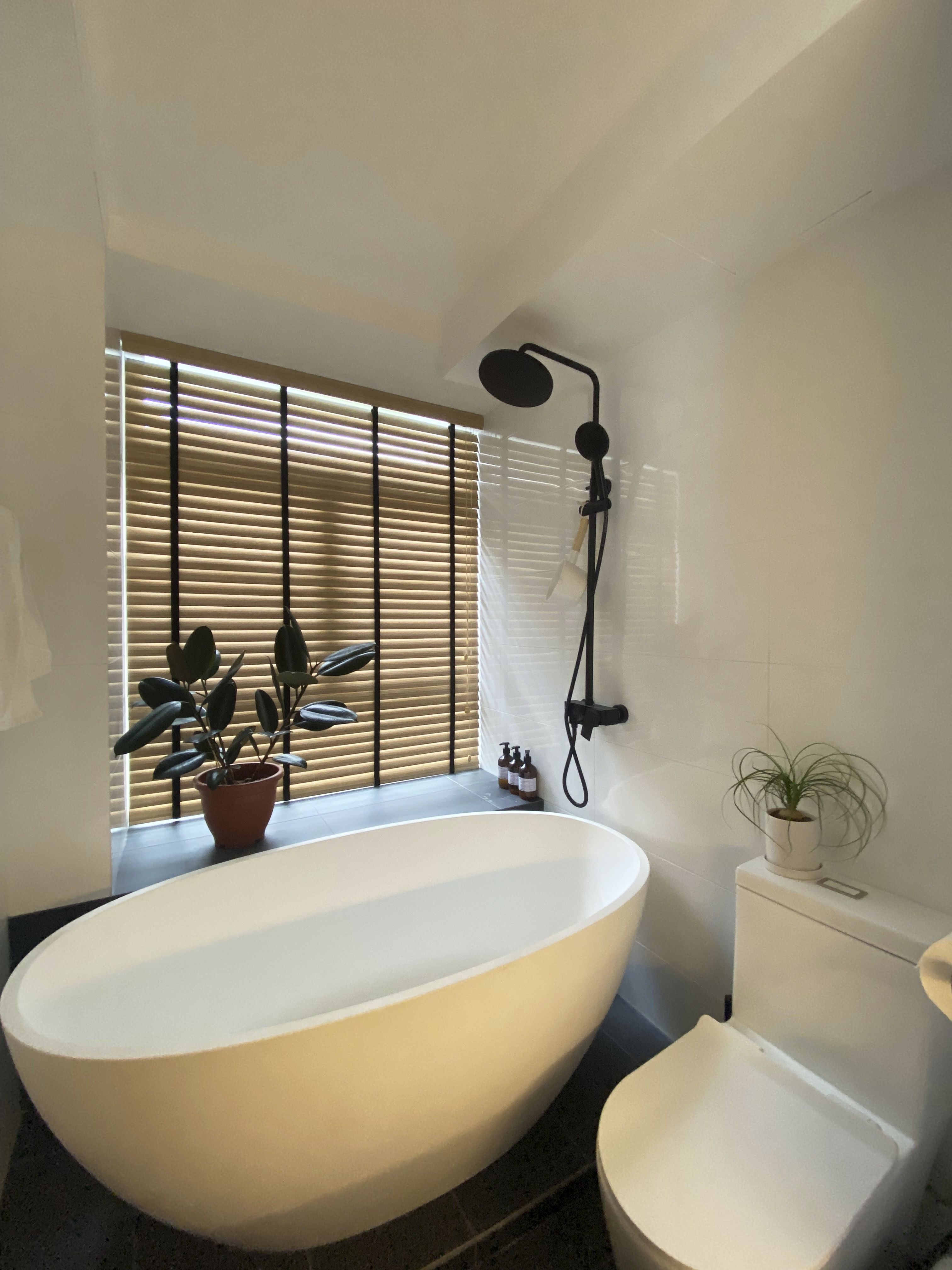 A Minimalist Apartment with an Urban Jungle - Modern minimalist bathroom, large oval bathtub, white ceramic sink, sleek black