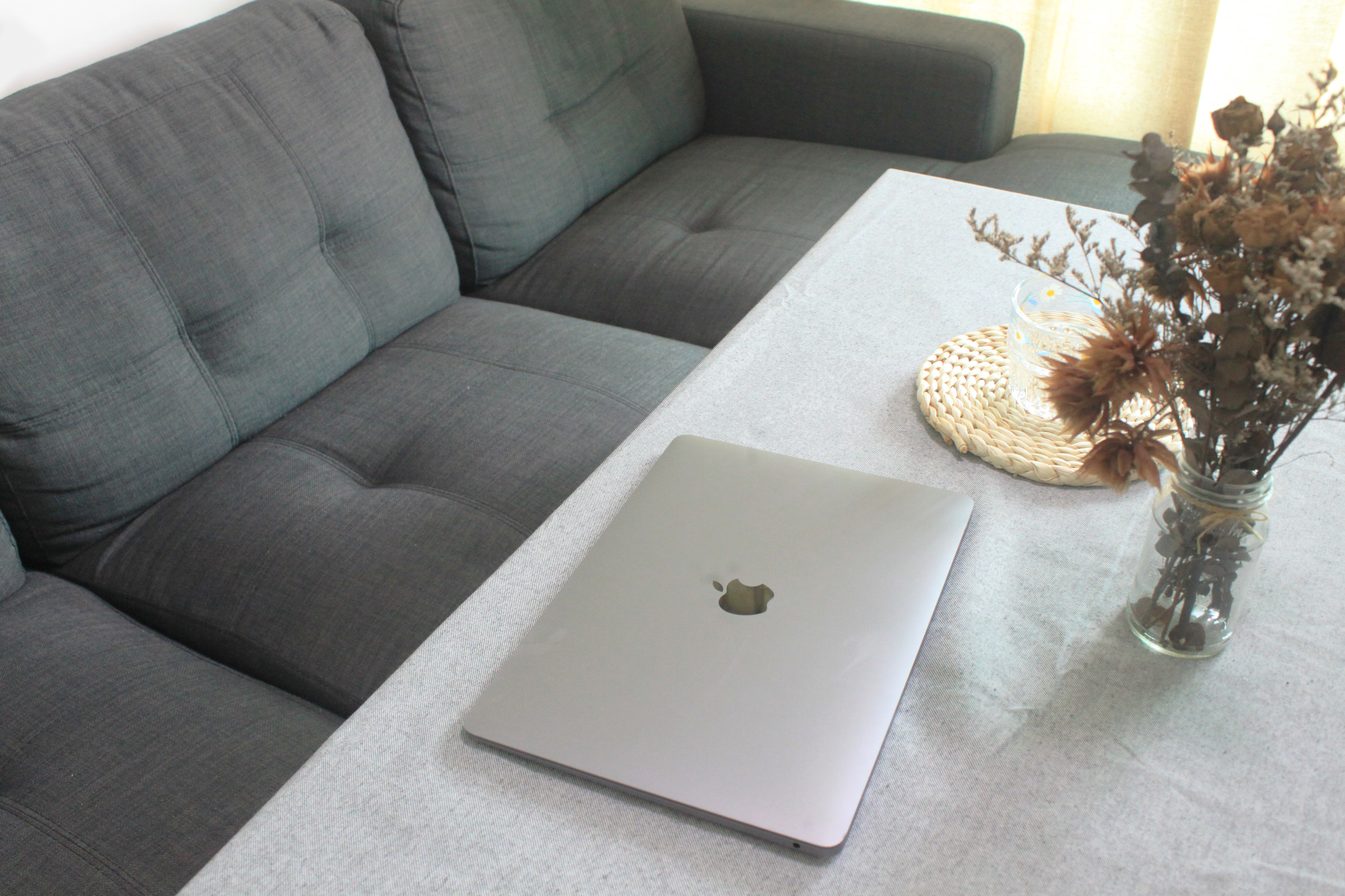 My Home Away From Home - Grey couch, gray cushions, light gray tablecloth, silver laptop, Apple logo, closed laptop, natural