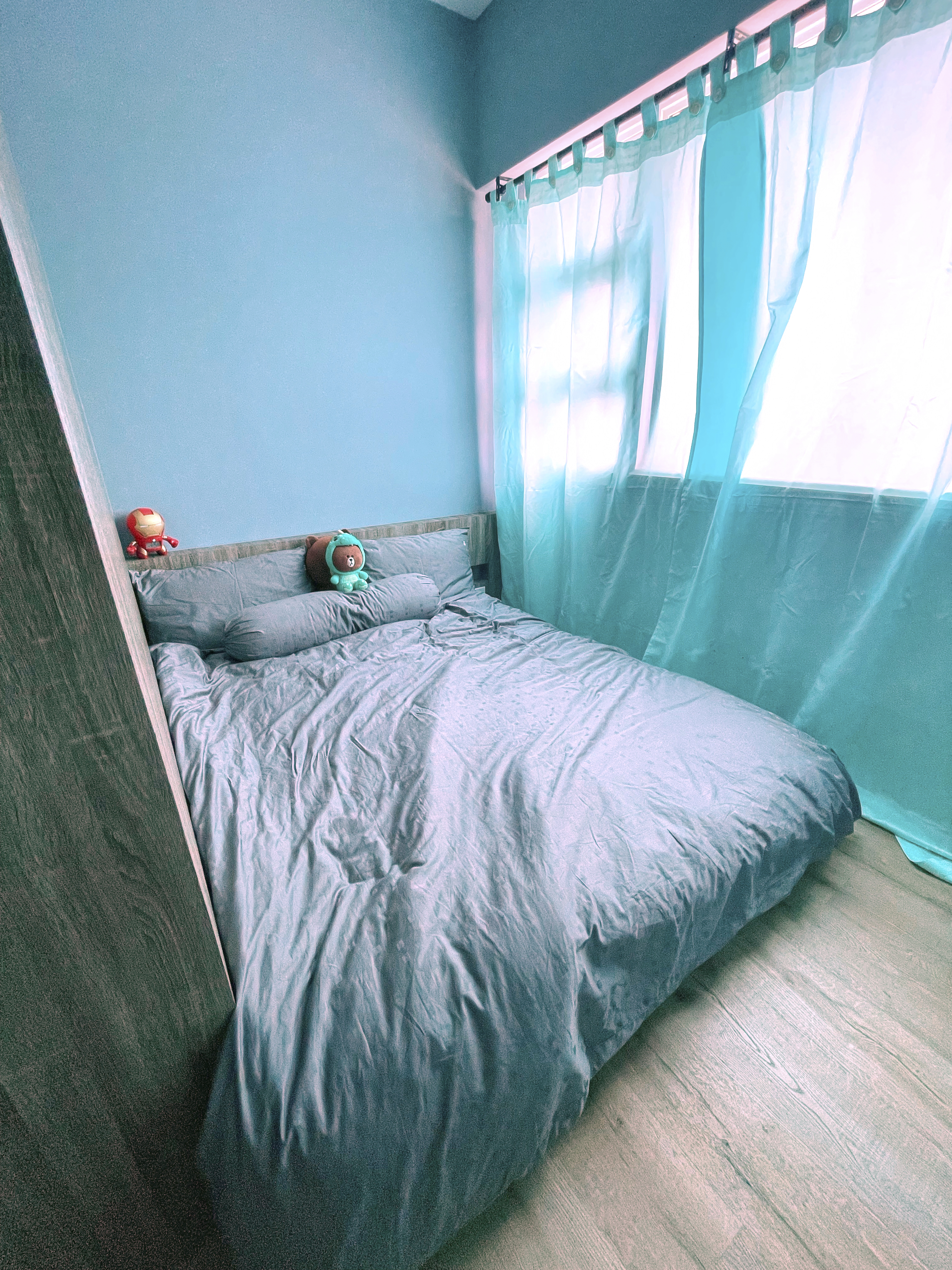 Our Colourful Personalities Imprinted On Our Apartment - Blue walls, teal curtains, bed with gray bedding, plush toys, wooden