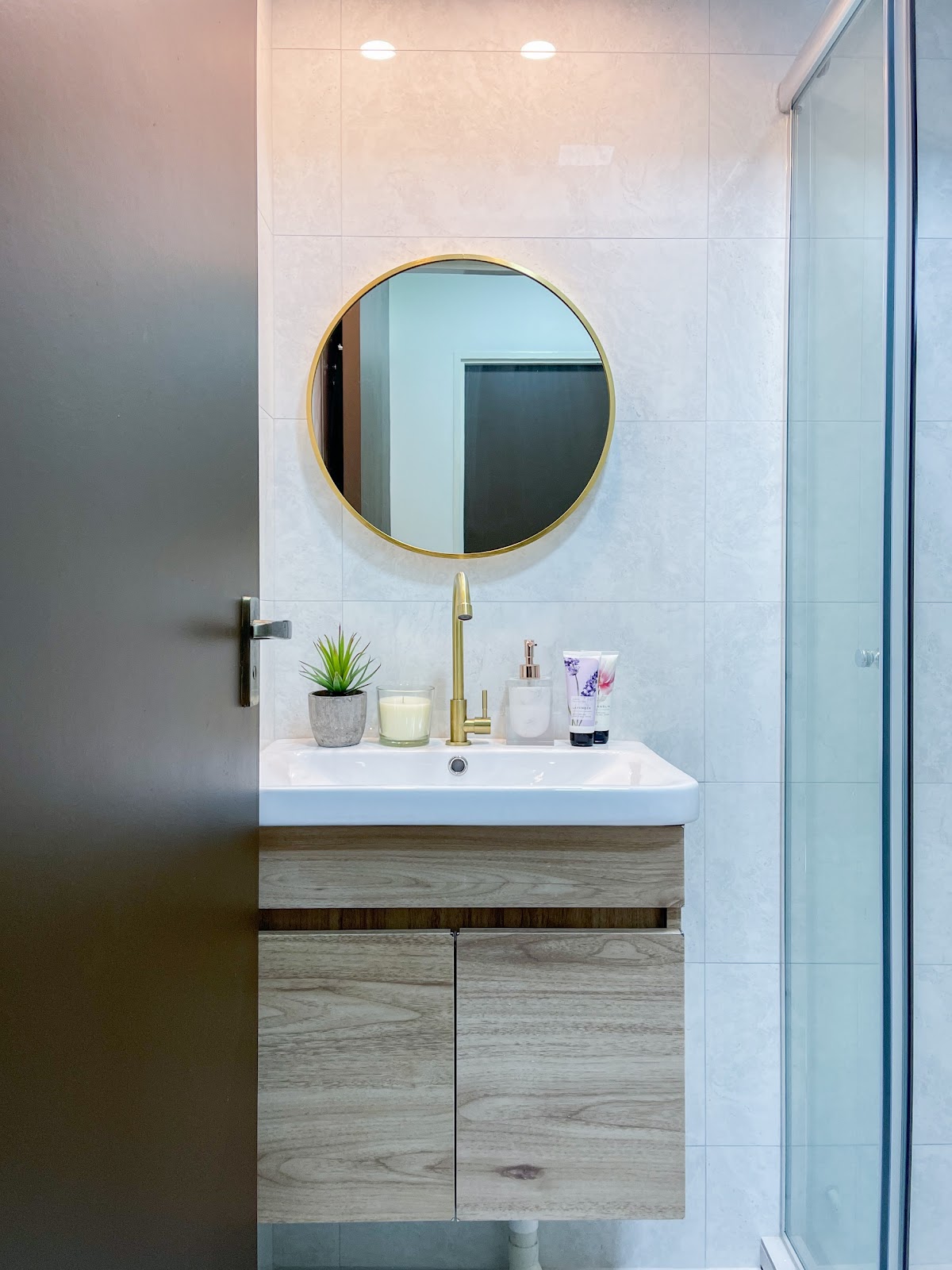 Modern Home for the Modern Interracial Couple - Round mirror with gold frame, white sink with gold faucet, wooden cabinet